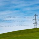 Transmission lines pictured on green hills with blue sky in the background.